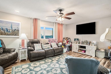Living room featuring a textured ceiling, wood finished floors, and a ceiling fan