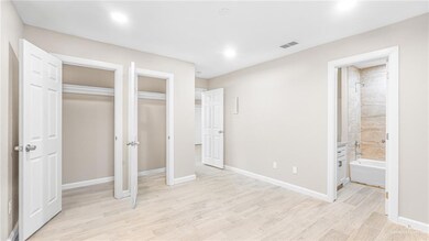 Unfurnished bedroom with light wood-style flooring, multiple closets, ensuite bathroom, and recessed lighting