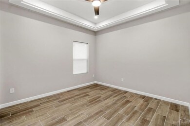 Empty room with a tray ceiling, wood finished floors, baseboards, and a ceiling fan