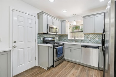 Kitchen with appliances with stainless steel finishes, gray cabinetry, light countertops, wood finished floors, and recessed lighting