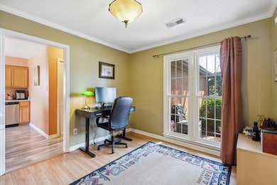 Home office featuring a textured ceiling, visible vents, light wood finished floors, baseboards, and ornamental molding