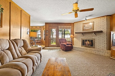 Carpeted living area with a brick fireplace, wooden walls, ceiling fan, and a textured ceiling