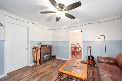 Living area with ornamental molding, wood finished floors, a wainscoted wall, a fireplace, and ceiling fan