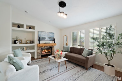 Living area with built in shelves, vaulted ceiling, wood finished floors, and a stone fireplace
