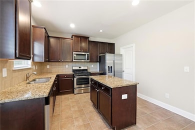 Kitchen featuring stainless steel appliances, dark brown cabinets, tasteful backsplash, light stone counters, and a kitchen island
