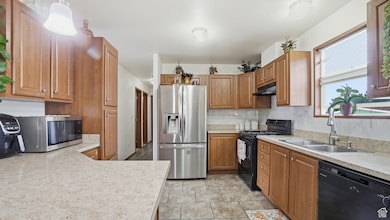 Kitchen featuring black appliances, brown cabinetry, light countertops, light tile patterned floors, and under cabinet range hood