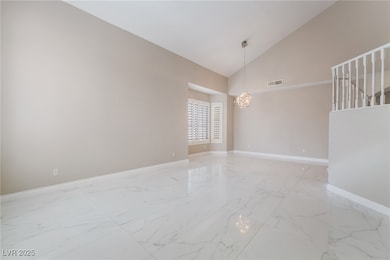 Empty room featuring high vaulted ceiling, light marble finish flooring, a chandelier, and stairway