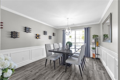 Dining room featuring a chandelier, wood finished floors, ornamental molding, wainscoting, and a decorative wall