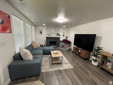 Living room with wood finished floors, a stone fireplace, and recessed lighting