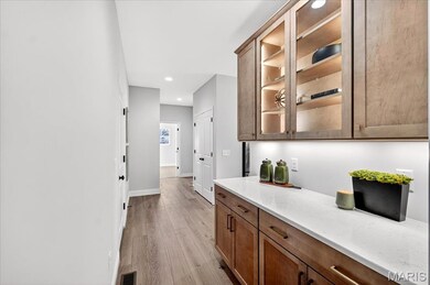 Butlers Pantry with light wood-style flooring, light stone countertops, glass insert cabinets, brown cabinets, and recessed lighting