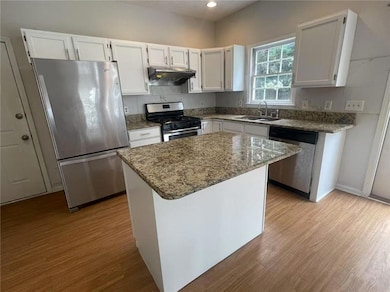 Kitchen with stainless steel appliances, under cabinet range hood, wood finished floors, stone counters, and recessed lighting