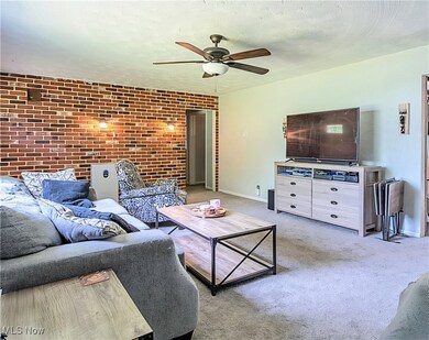 Carpeted living room with ceiling fan and brick wall