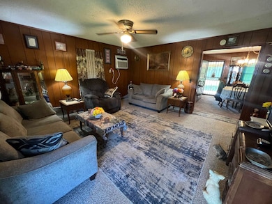 Carpeted living room featuring wood walls, an AC wall unit, a textured ceiling, and ceiling fan