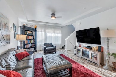 Living area featuring a raised ceiling, a ceiling fan, stairway, and wood finished floors