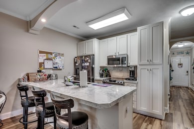 Kitchen with arched walkways, ornamental molding, a peninsula, decorative backsplash, and light wood-type flooring