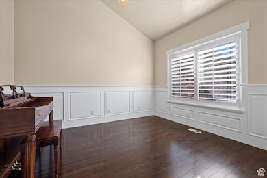Unfurnished dining area with a decorative wall, wainscoting, lofted ceiling, and dark wood-type flooring