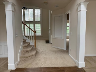 Carpeted foyer with ornate columns, a ceiling fan, stairs, and wood finished floors