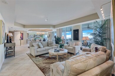 Living room featuring a raised ceiling, light tile patterned flooring, and ceiling fan with notable chandelier