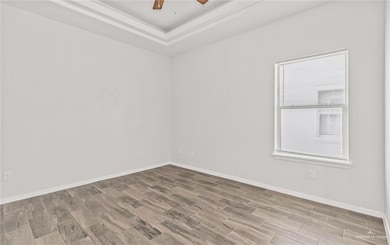 Empty room featuring baseboards, a tray ceiling, ceiling fan, and wood finished floors