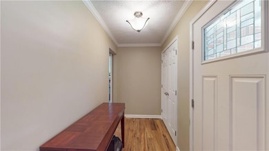 Entryway with light wood-style flooring, a textured ceiling, and crown molding