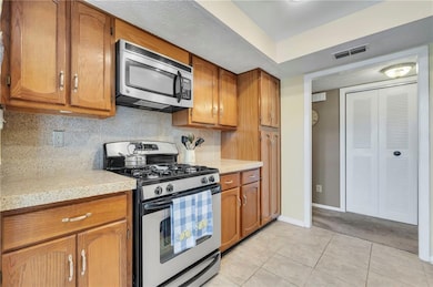 Kitchen with tasteful backsplash, stainless steel appliances, light colored carpet, and light stone counters