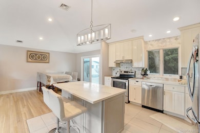 Kitchen featuring stainless steel appliances, decorative backsplash, a kitchen island, decorative light fixtures, and a kitchen breakfast bar