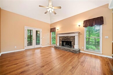 Unfurnished living room featuring a ceiling fan, light wood-style flooring, a stone fireplace, and baseboards