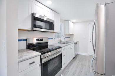 Kitchen with appliances with stainless steel finishes, tasteful backsplash, light wood finished floors, white cabinets, and light stone counters