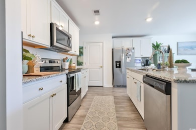 Kitchen featuring stainless steel appliances, white cabinets, light stone countertops, a center island with sink, and recessed lighting