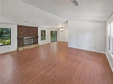 Unfurnished living room with a chandelier, plenty of natural light, wood finished floors, a fireplace, and a textured ceiling