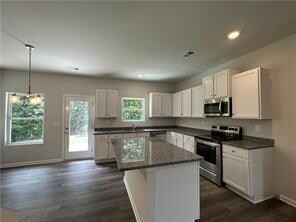 Kitchen featuring stainless steel appliances, dark countertops, dark wood-type flooring, recessed lighting, and a kitchen island