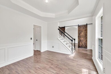 Empty room with a barn door, a tray ceiling, healthy amount of natural light, wood finished floors, and wainscoting