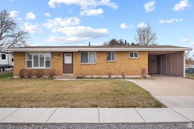 Ranch-style home with brick siding, a carport, concrete driveway, and a front lawn