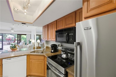 Kitchen featuring stainless steel appliances, track lighting, open floor plan, light stone counters, and light tile patterned flooring
