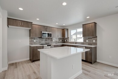 Kitchen featuring decorative backsplash, appliances with stainless steel finishes, light stone countertops, a center island, and light wood-style flooring