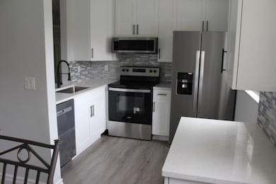 Kitchen featuring stainless steel appliances, backsplash, light stone countertops, and white cabinets