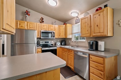 Kitchen featuring appliances with stainless steel finishes, lofted ceiling, light brown cabinets, light countertops, and light tile patterned floors