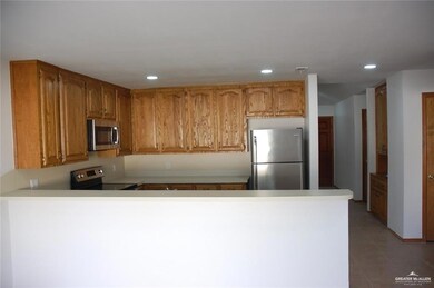 Kitchen with brown cabinets, stainless steel appliances, recessed lighting, light countertops, and a peninsula