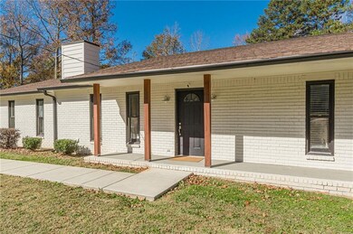 View of front of house with brick siding, a porch, a front lawn, a chimney, and a shingled roof