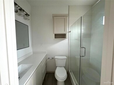 Full bath featuring toilet, vanity, a stall shower, wood finished floors, and baseboards