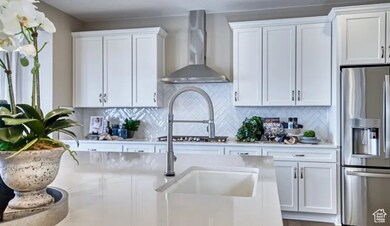 Kitchen with stainless steel fridge with ice dispenser, white cabinets, tasteful backsplash, and wall chimney exhaust hood