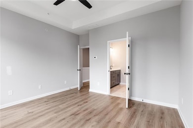 Unfurnished bedroom with light wood-type flooring, baseboards, ensuite bath, and a ceiling fan