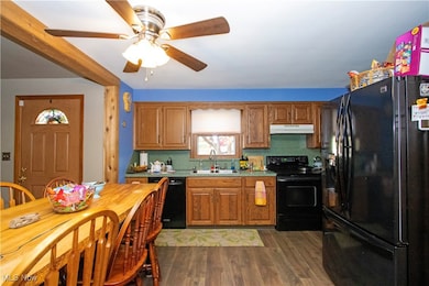Kitchen featuring black appliances, brown cabinets, dark wood-style floors, light countertops, and under cabinet range hood