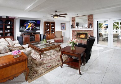 The expansive family room with its beamed ceilings, lighted ceiling fan, floor-to-ceiling brick fireplace with updated brass enclosure, recently renewed wet-bar with showcase cabinetry and elegant French doors that lead to the patio is perfect for fa