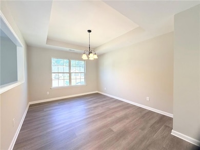 Unfurnished dining area with a tray ceiling, dark wood finished floors, and a chandelier