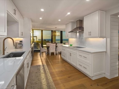 Kitchen with white cabinets, dark wood-style floors, recessed lighting, wall chimney exhaust hood, and pendant lighting
