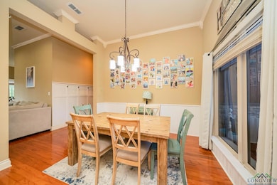 Dining space with crown molding, wood finished floors, a chandelier, and wainscoting
