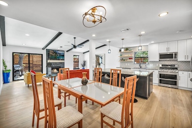 Dining space with light wood-style floors, recessed lighting, a ceiling fan, a chandelier, and a fireplace
