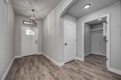 Foyer with arched walkways, wood finished floors, baseboards, and a chandelier