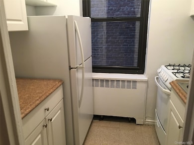 Kitchen with white cabinetry, white appliances, and radiator
